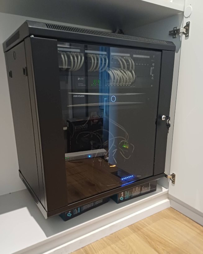 A wall-mounted glass-fronted network cabinet installed by GreyX, with blue patch cables routed neatly to a switch