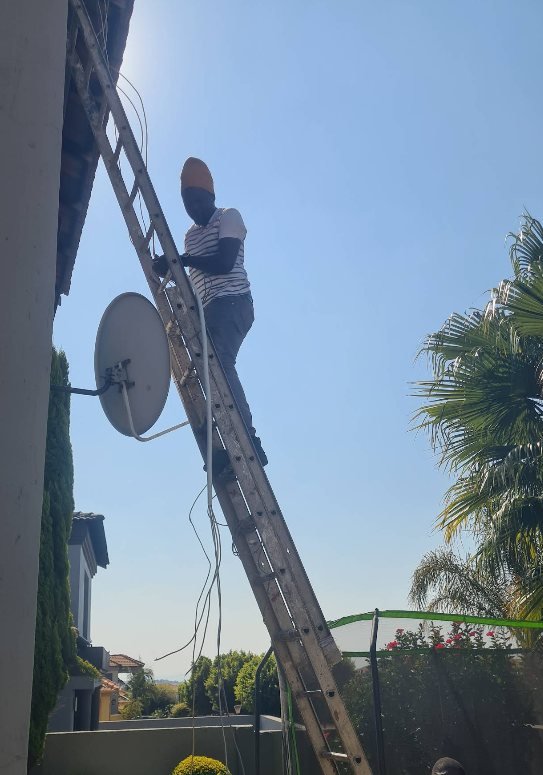 A GreyX technician on an extension ladder working at a roof-mounted satellite dish