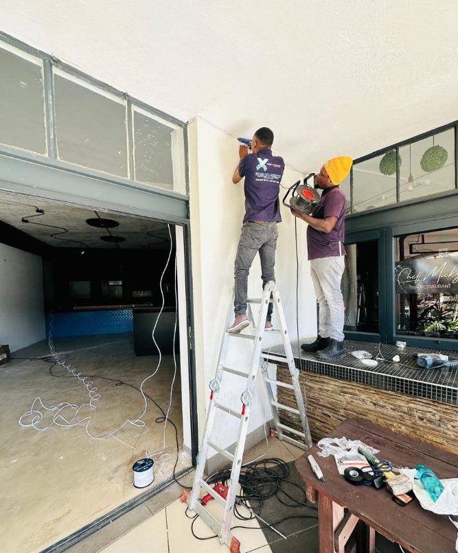 Two GreyX technicians on ladders installing cabling in an empty commercial shopfront