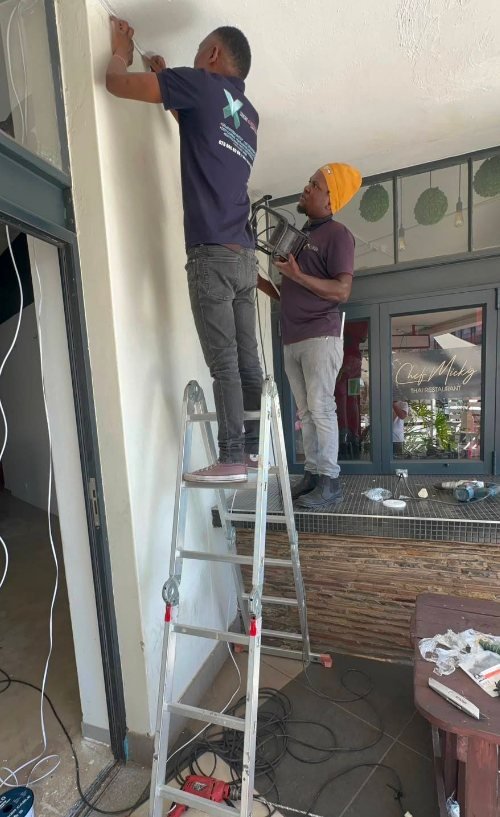 Two GreyX technicians in branded shirts working together, one on a step ladder running cable