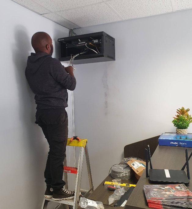 A GreyX technician mounting network equipment onto an interior wall beside a router
