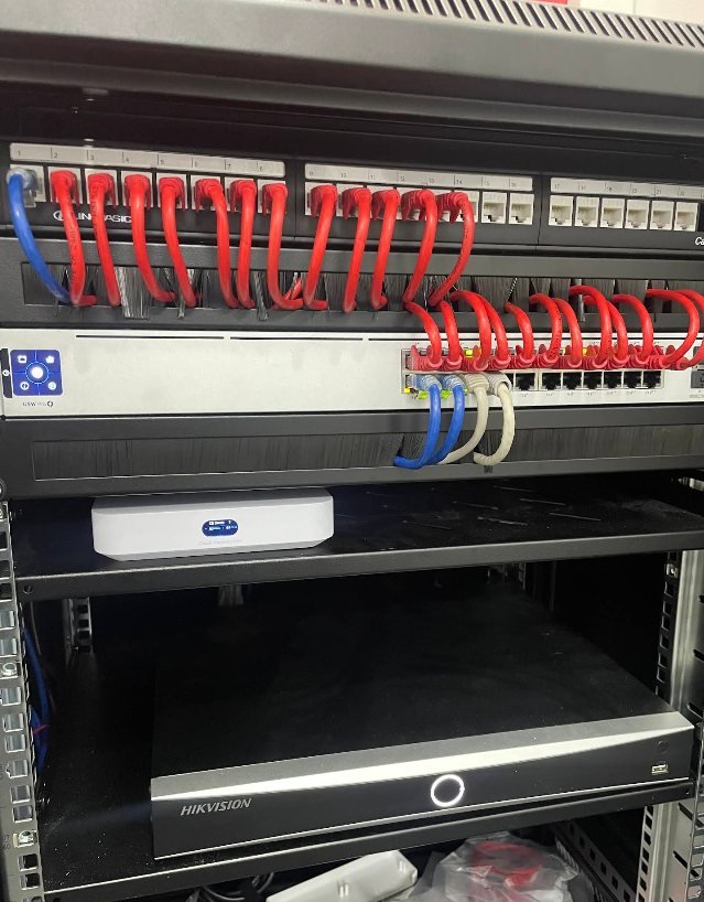 A network rack with a red and white patch panel above a Hikvision CCTV recorder