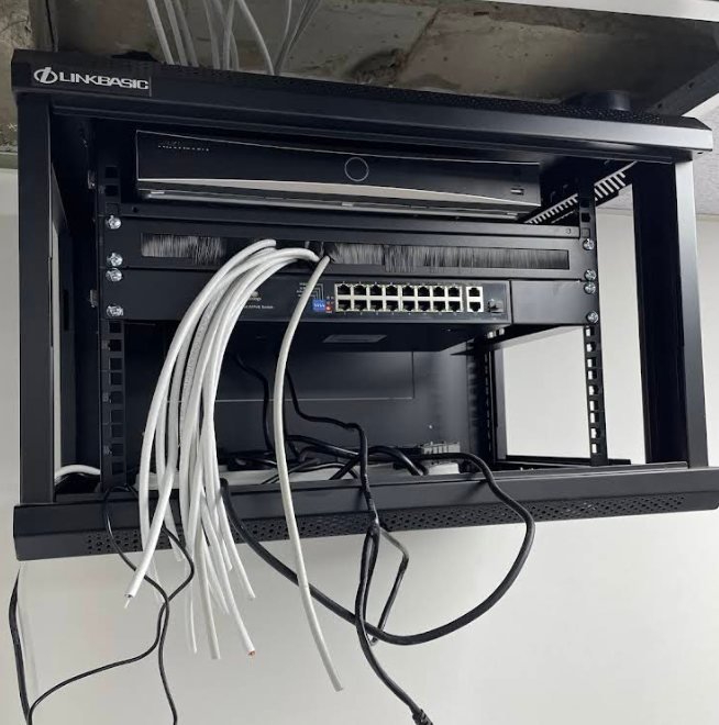 A wall-mounted network cabinet with white patch cables running down to two switches